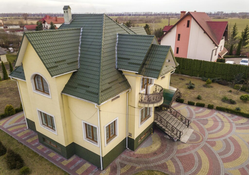 Aerial top view of new residential house cottage with shingle roof on fenced big yard on sunny day.