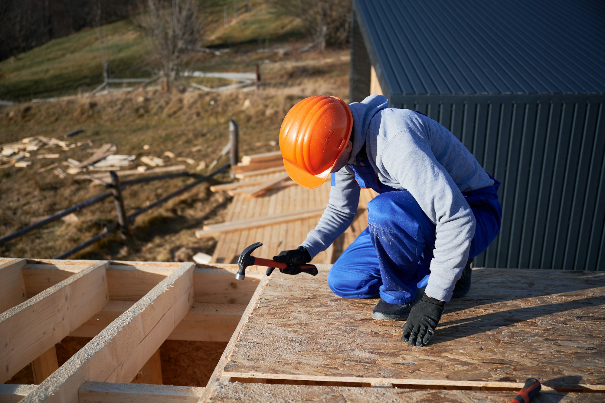 Carpenter hammering nail into OSB panel while building wooden frame house.