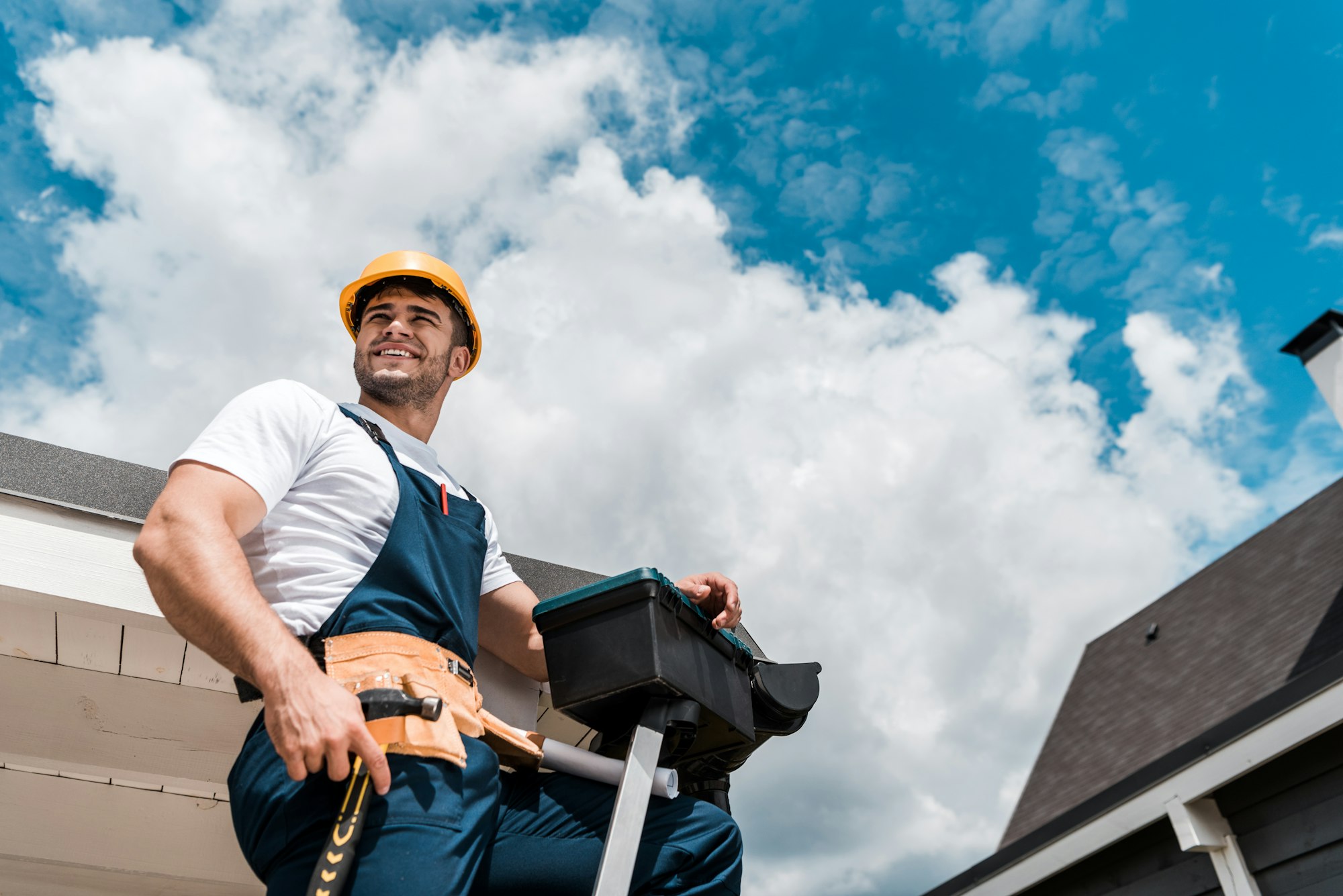 low angle view of happy repairman in helmet holding hammer and toolbox