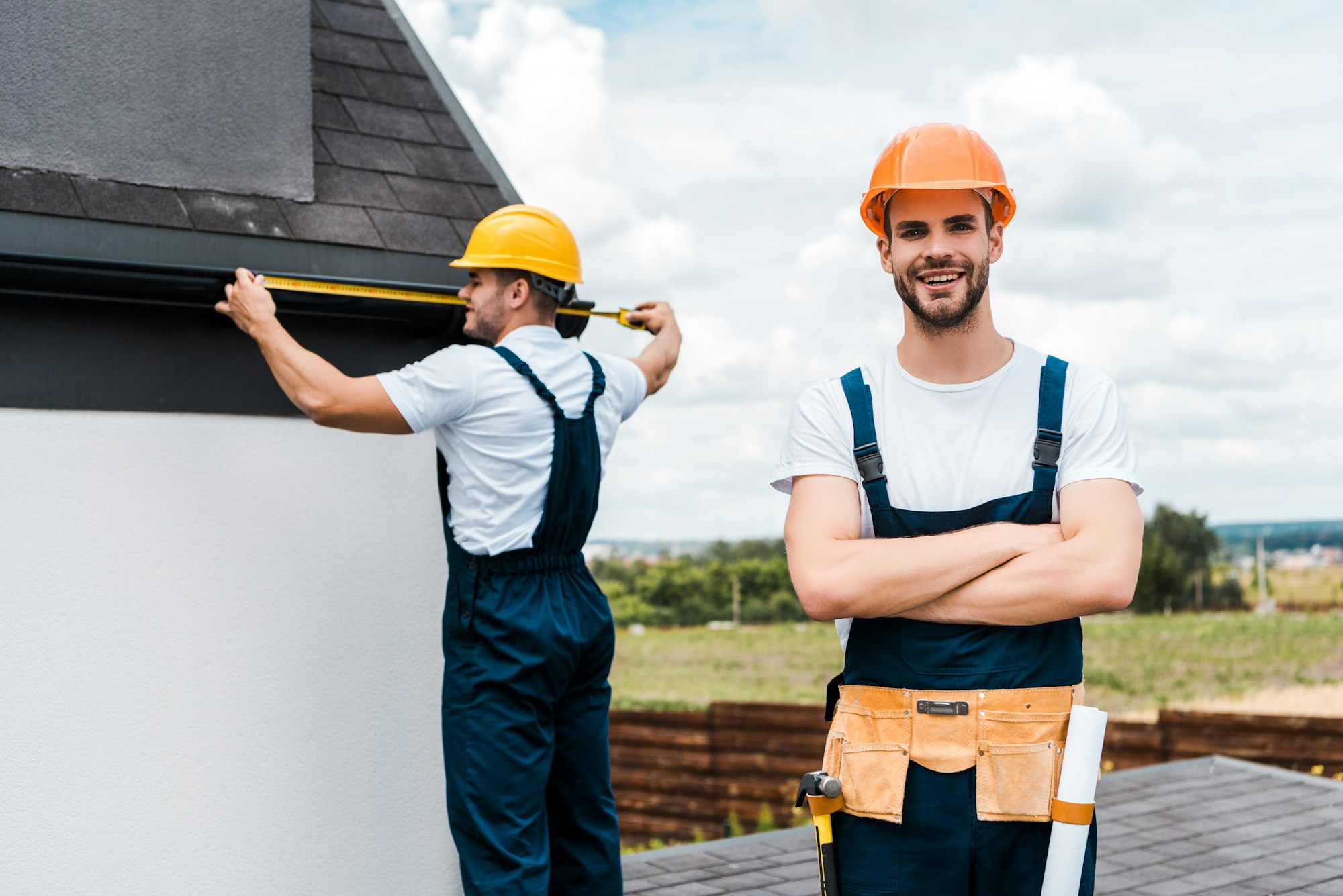 selective focus of happy repairman standing with crossed arms and smiling near coworker